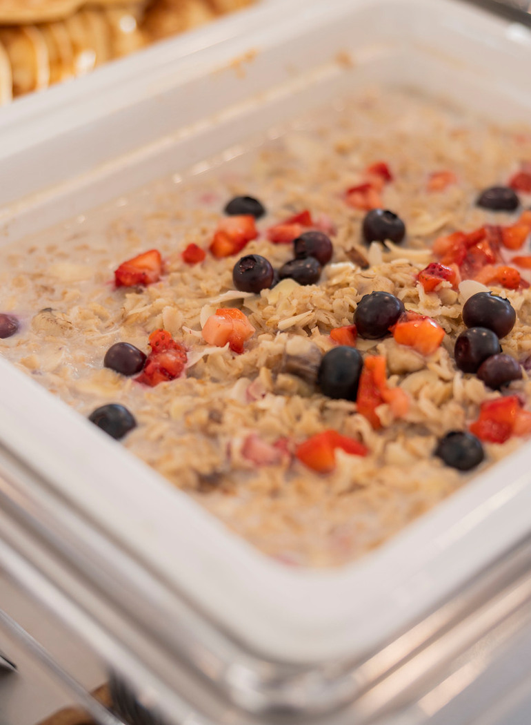Cremiger Haferbrei mit Heidelbeeren, gewürfelten Erdbeeren und Mandelblättchen im Frühstücksbuffet; Pfannkuchen daneben.