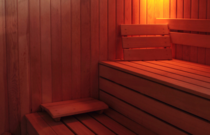 Sauna hotelowa wyłożona drewnem, z piętrowymi ławkami, oparciem i ciepłym bursztynowym oświetleniem do relaksu