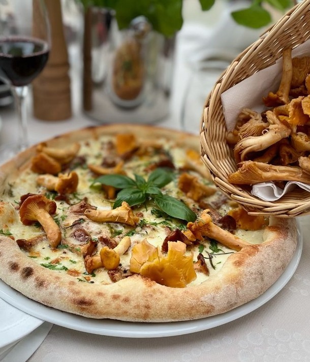 Pizza z pieca z kurkami i bazylią, koszyk świeżych kurek i kieliszek czerwonego wina