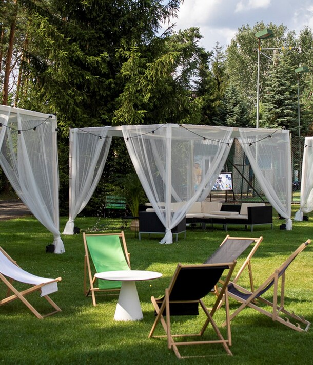 Hotelowy ogród z białymi, tiulowymi kabinami, lampkami, sofami i leżakami na trawniku do relaksu na świeżym powietrzu