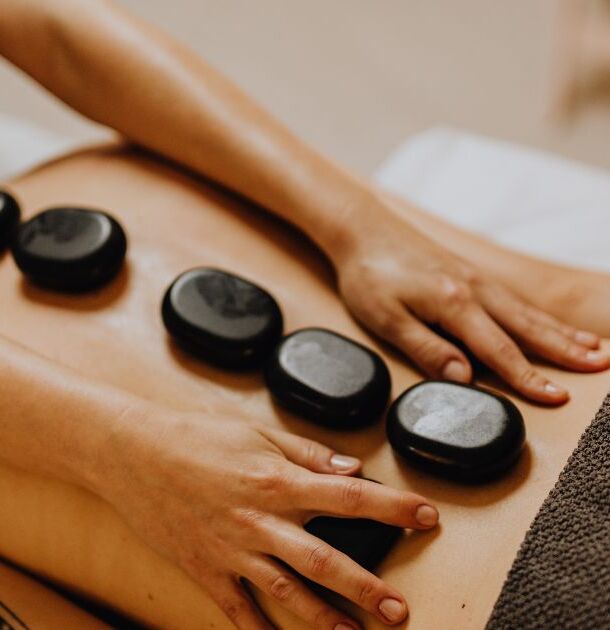 Zabieg spa z gorącymi kamieniami bazaltowymi ułożonymi wzdłuż kręgosłupa, dłonie personelu spa, relaksujący masaż