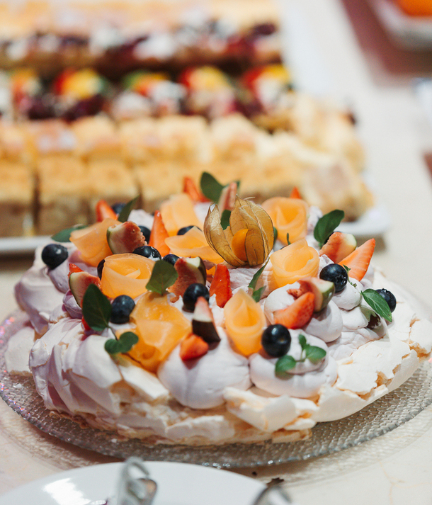 Pavlova na deserowym bufecie, udekorowana różami z brzoskwiń, truskawkami, borówkami i miechunką
