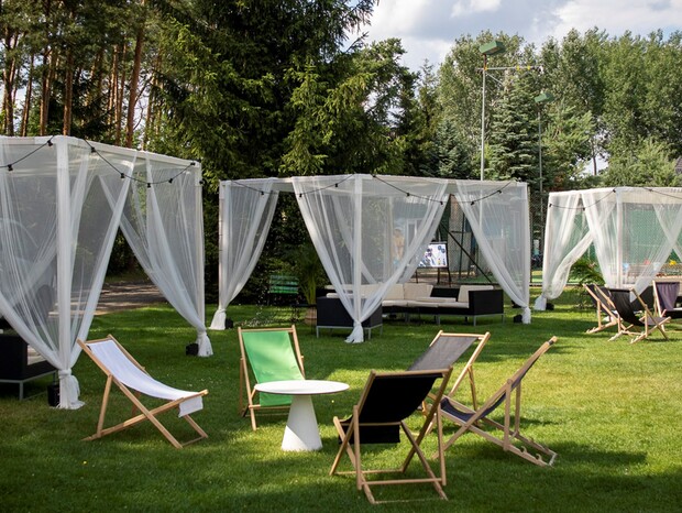 Hotelowy ogród z białymi, tiulowymi kabinami, lampkami, sofami i leżakami na trawniku do relaksu na świeżym powietrzu