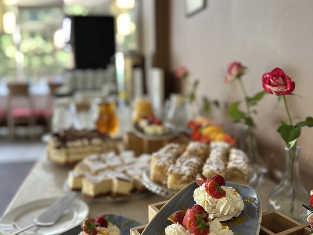 Bufet deserowy: bezy Pavlova z bitą śmietaną i świeżymi truskawkami, różnorodne ciasta i pojedyncze róże na stole.