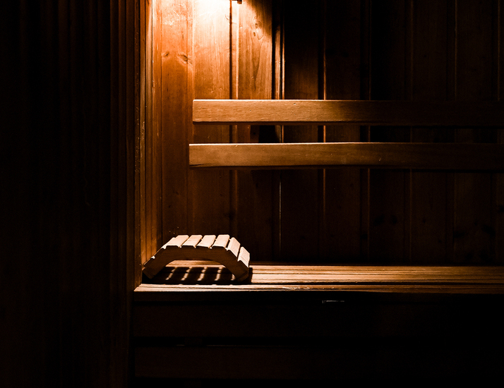 Przytulna hotelowa sauna z piętrowymi drewnianymi ławkami, drewnianymi podpórkami i ciepłym, nastrojowym oświetleniem