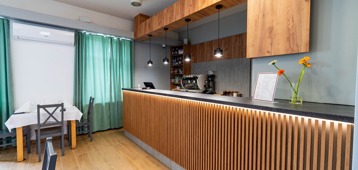 Modern breakfast bar with wooden slatted counter, pendant lamps, coffee machine, menu and flowers.