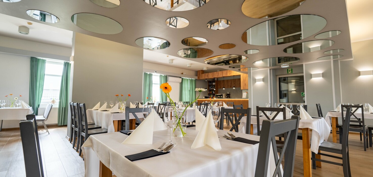 Modern hotel restaurant with white tablecloths, folded napkins, gerberas in vases and round mirrored ceiling panels.
