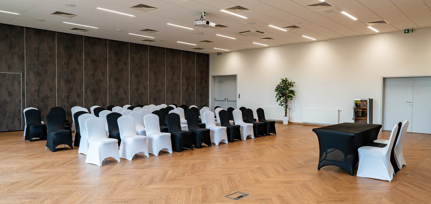 Nowoczesna sala konferencyjna z czarno-białymi pokrowcami na krzesłach, projektorem sufitowym i parkietem