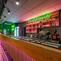 Stylowy bar hotelowy z długim drewnianym barem, neonem na zdrowie, podświetlonymi półkami z alkoholem i zieloną ścianą