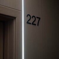 Nowoczesne drzwi hotelowe z drewnianymi panelami, pionową listwą LED i czarnym numerem pokoju 227
