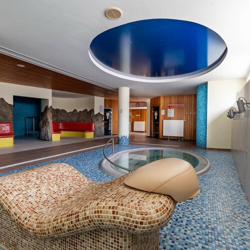Hotel spa with mosaic loungers, round jacuzzi, blue ceiling and red seats