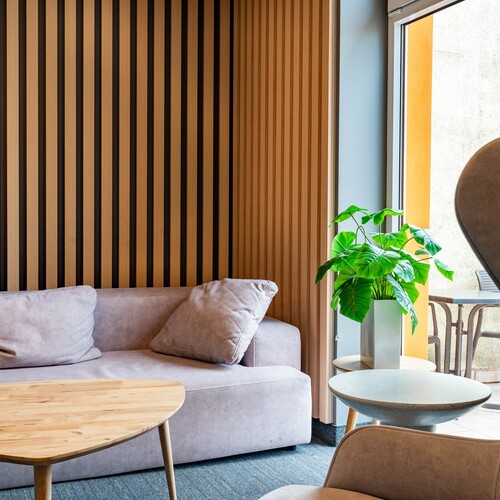 Cozy corner with a beige sofa, wood-slat wall, plant by the window and round tables