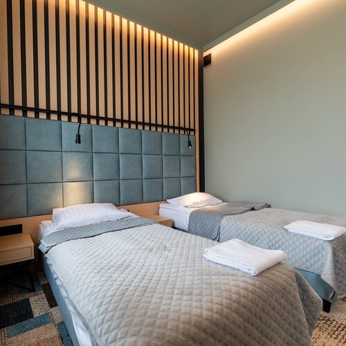 Room with two single beds, upholstered headboard, bedside table, reading lamps and subtle lighting.