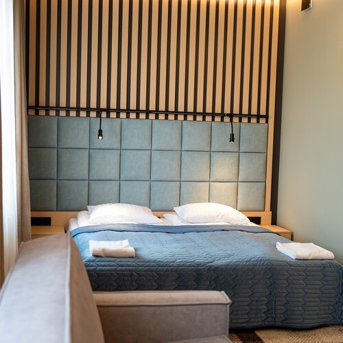 King bed with quilted turquoise headboard, vertical wood slats, adjustable bedside lamps and folded towels