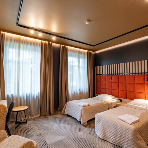 Twin room with two single beds, quilted bedspreads, warm orange headboard, sheer curtains, desk, armchair and mood lighting