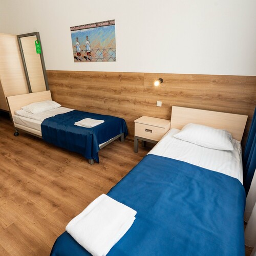Bright room with two single beds, blue bedspreads, towels, wooden headboard, wardrobe and blue curtains.