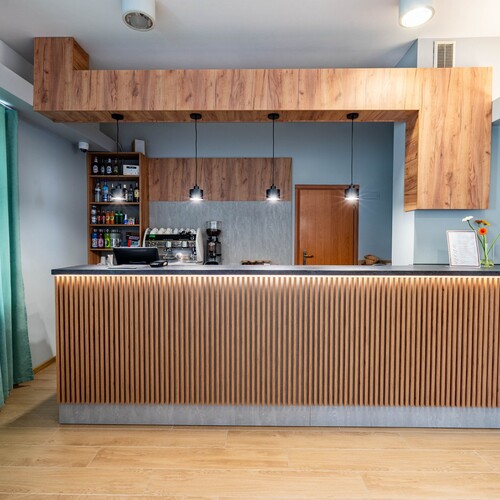 Hotel reception with café: wood-slat front, pendant lamps, coffee machine, drink shelves and turquoise curtains.