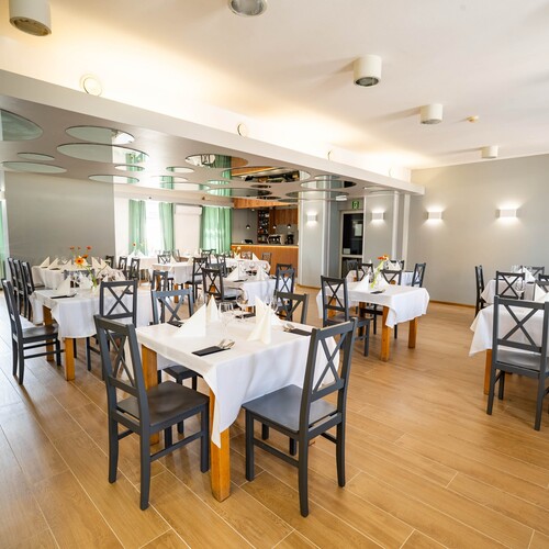 Bright hotel restaurant with white tablecloths, wooden floor, green curtains, mirrored round panels and bar.