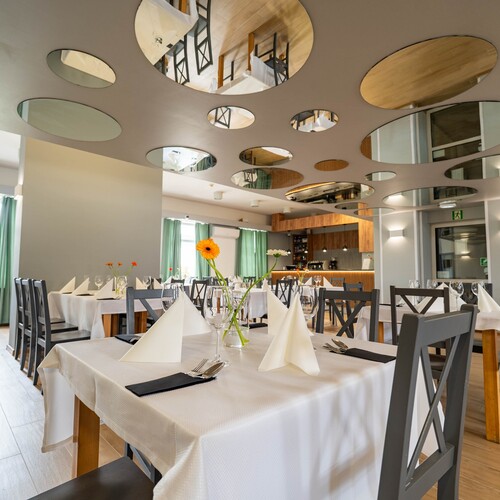 Modern hotel restaurant with white tablecloths, folded napkins, gerberas in vases and round mirrored ceiling panels.