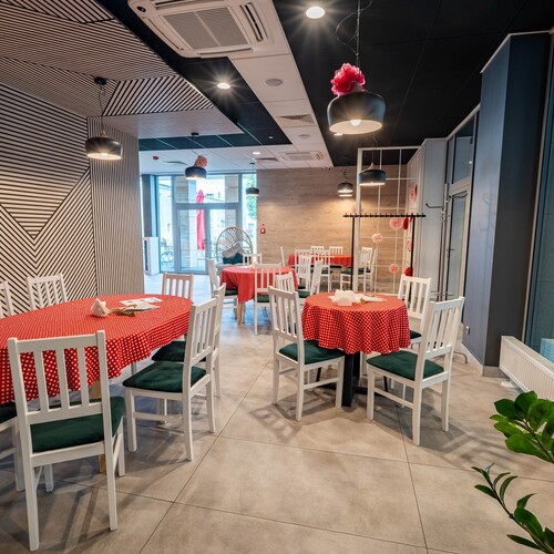 Hotel bistro with round tables covered in red and white polka-dot cloths, white chairs with green cushions, pendant lamps and striped wall