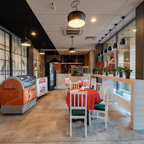 Modern hotel café with red polka-dot tablecloths, white chairs, pendant lamps, freezer and plants.