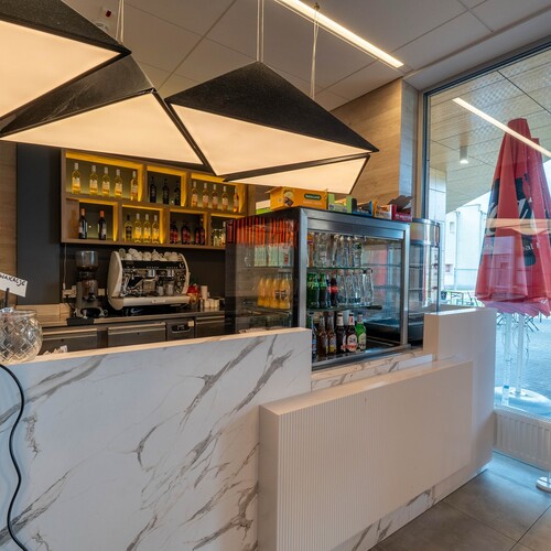 Modern Karmel hotel café: marble bar, geometric lamps, coffee machine and illuminated drink shelves.