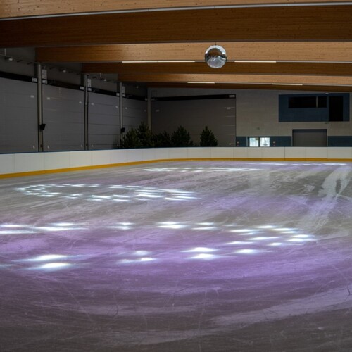 Indoor ice rink with wooden ceiling beams and disco ball, purple-white lights on the ice — ideal for hotel attractions.