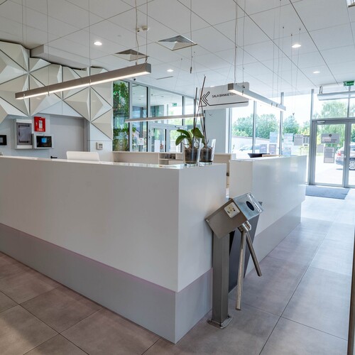 Bright modern hotel reception with elegant white desk, geometric 3D panels, pendant lamps and orchids