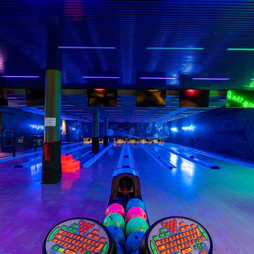 Neon hotel bowling alley with several lanes, colorful balls, overhead screens and a bar for evening relaxation.