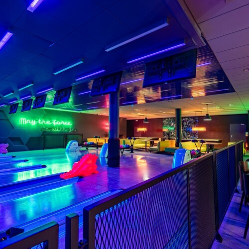Neon hotel bowling room with colorful lanes, booths, ball returns and 'May the force be with you' neon