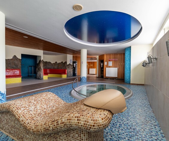 W hotelowym spa z mozaikowymi leżankami, okrągłym jacuzzi, niebieskim sufitem i czerwonymi siedziskami