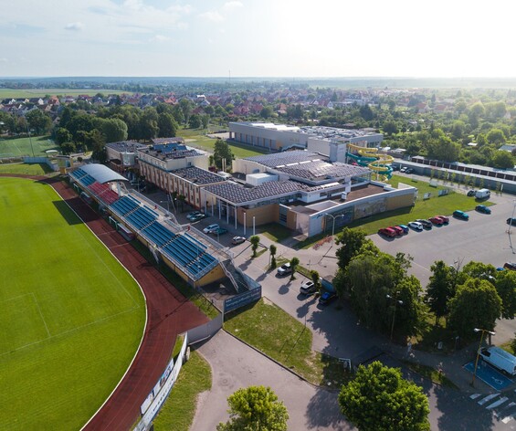 Kompleks sportowo-rekreacyjny z zielonym boiskiem, zadaszonymi trybunami, aquaparkiem z żółtymi zjeżdżalniami i panelami słonecznymi