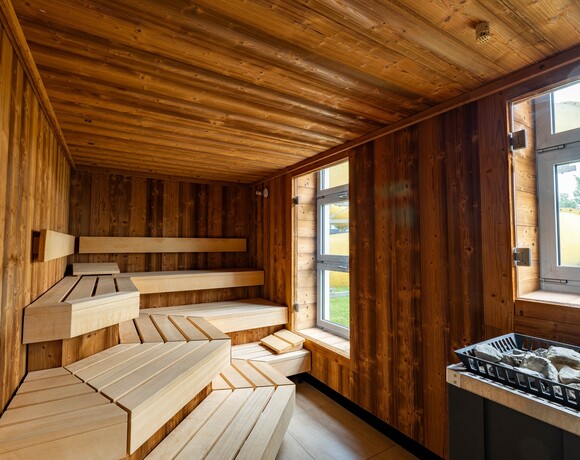 Hotelowa sauna wyłożona drewnem z wielopoziomowymi ławkami, piecem na kamienie i oknem z widokiem