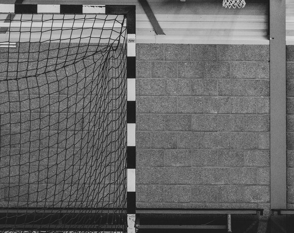 Hala sportowa z obręczą do koszykówki zamocowaną na ścianie i bramką z siatką, metalowe belki i polerowana podłoga