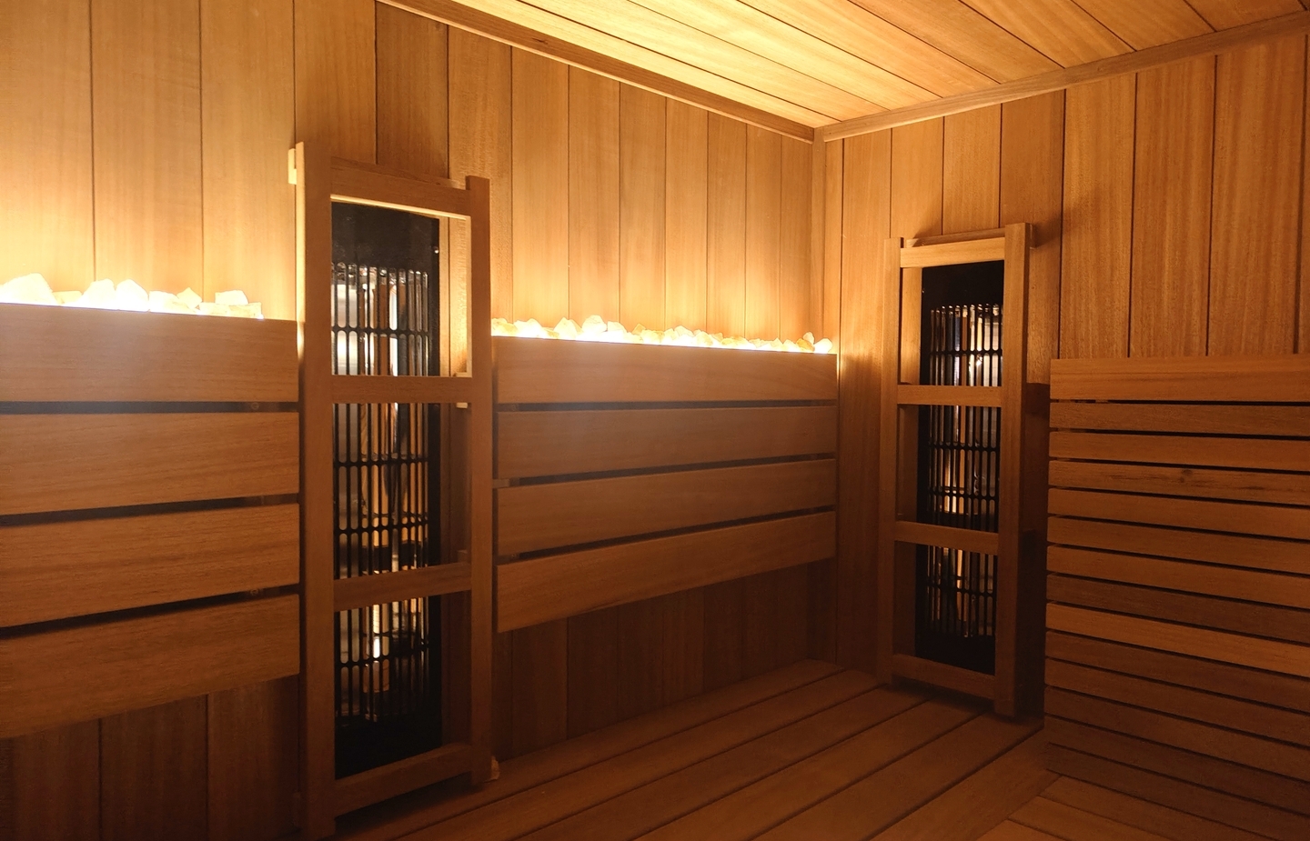 Sauna spa z drewnianymi ławkami, ciepłym nastrojowym oświetleniem i kamieniami grzewczymi na tylnej półce