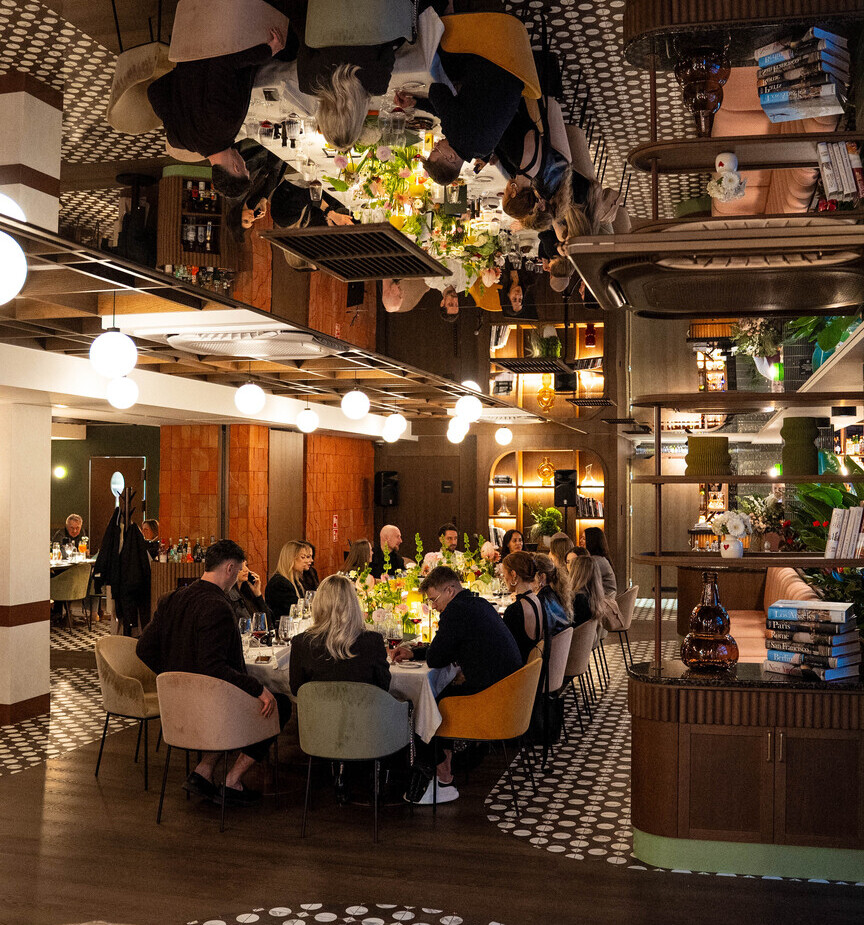 Elegancka restauracja hotelowa z długim stołem, goście przy kolacji, kwiatowe dekoracje i ciepłe oświetlenie