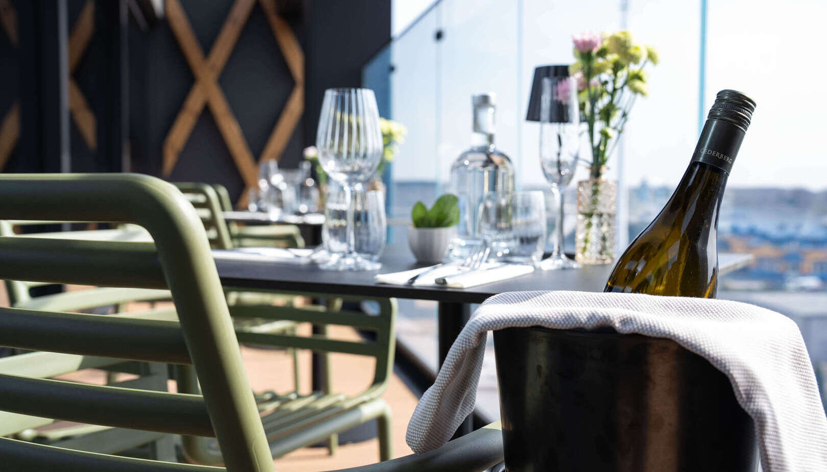 Tarasowy stolik restauracyjny z kieliszkami, bukietem kwiatów, zielonymi krzesłami i butelką w wiaderku przykrytą serwetą, widok na miasto.
