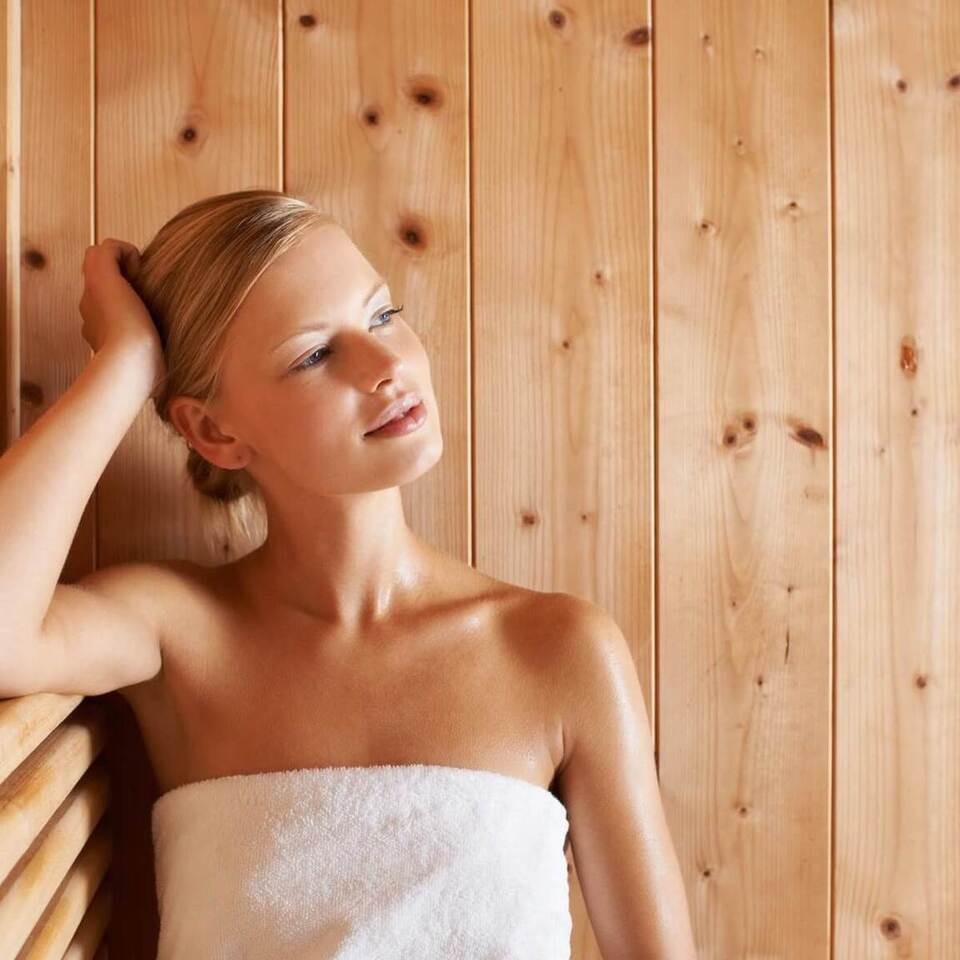 Kobieta owinięta ręcznikiem odpoczywa na ławce w drewnianej saunie hotelowej, ciepła, relaksująca atmosfera spa
