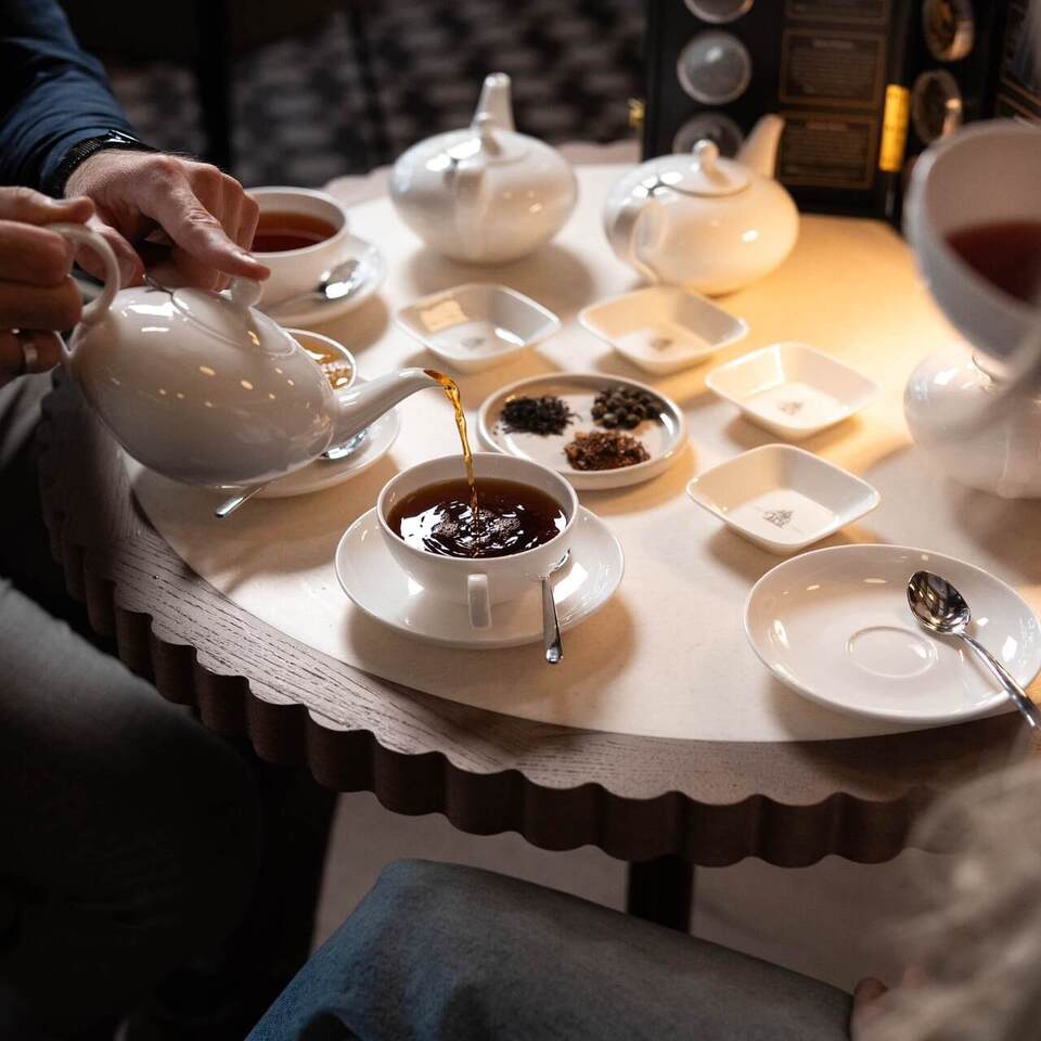 Hotelowy serwis herbaciany: biała porcelana, herbata nalewana do filiżanki i talerzyki z wyborem liści herbaty.