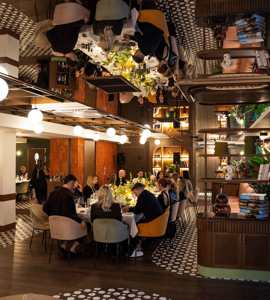 Elegancka restauracja hotelowa z długim stołem, goście przy kolacji, kwiatowe dekoracje i ciepłe oświetlenie