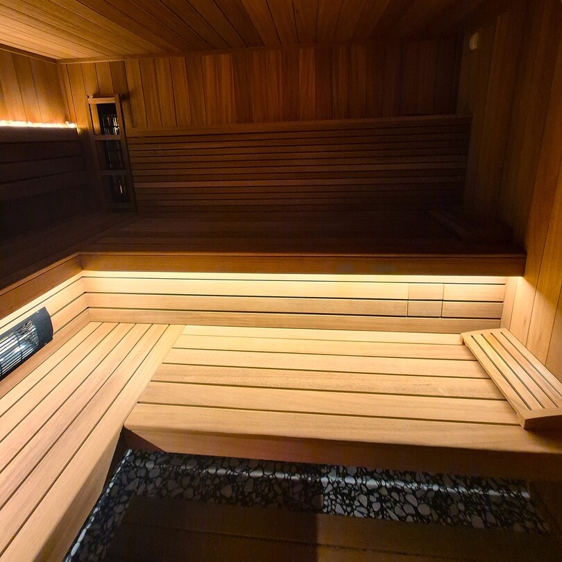 Sauna hotelowa z drewnianymi, wielopoziomowymi ławami, ciepłym ukrytym oświetleniem LED i piecem z kamieniami