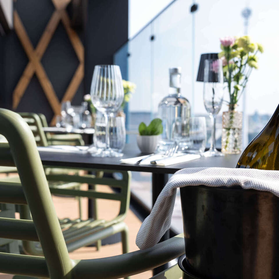 Tarasowy stolik restauracyjny z kieliszkami, bukietem kwiatów, zielonymi krzesłami i butelką w wiaderku przykrytą serwetą, widok na miasto.