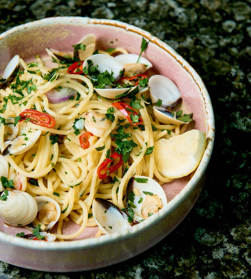 Spaghetti z małżami w oliwie, posypane świeżą pietruszką i chili, plasterek cytryny, podane w różowej misce