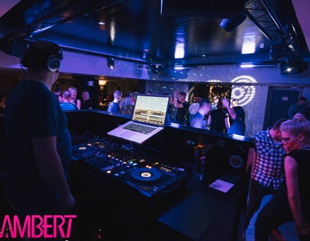 DJ gra muzykę w mrocznym klubie z kolorowym oświetleniem, goście tańczą i bawią się na parkiecie