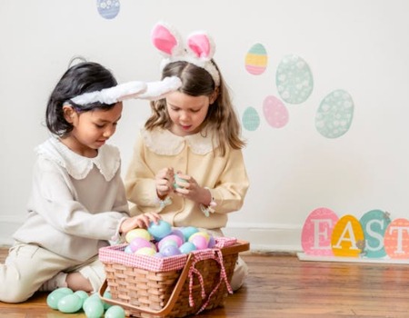 Zwei Kinder in einem Hotelzimmer spielen mit pastellfarbenen Ostereiern aus einem Korb, Osterdeko an der Wand