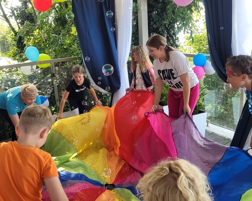 Children playing under a canopy with colorful fabric and soap bubbles at a hotel’s lively kids' event.