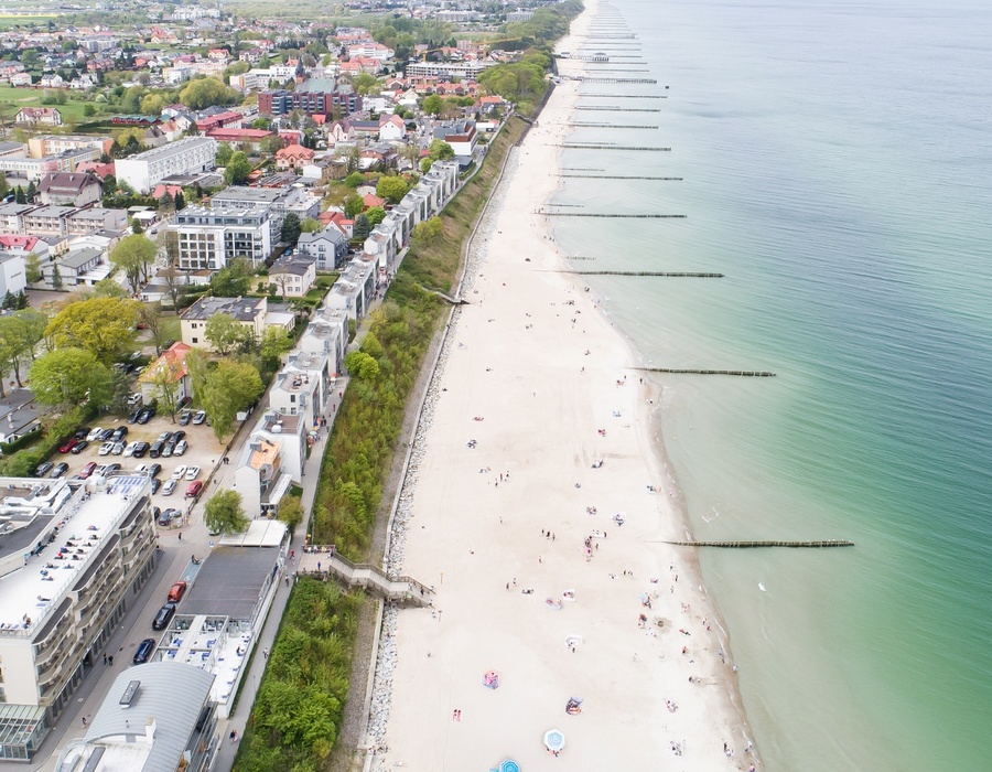Hotele i nowoczesne apartamenty przy piaszczystej plaży z promenadą, parasolami, falochronami i turkusowym morzem.