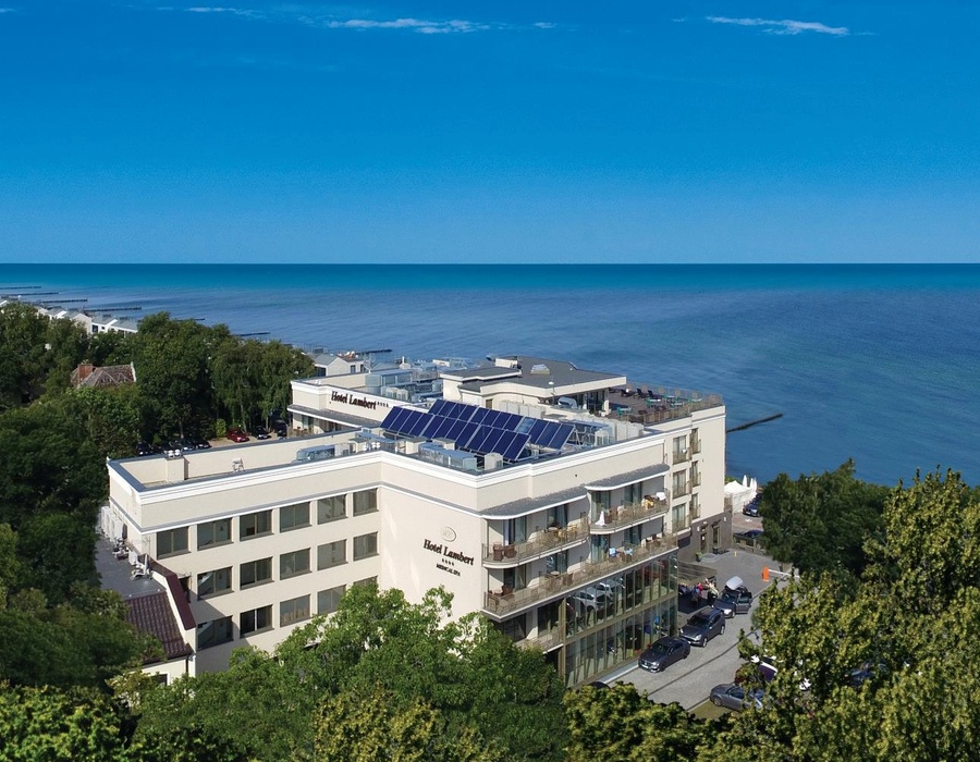 Hotel Lambert nad morzem z balkonami i widokiem na plażę, otoczony zielenią i spokojną zatoką
