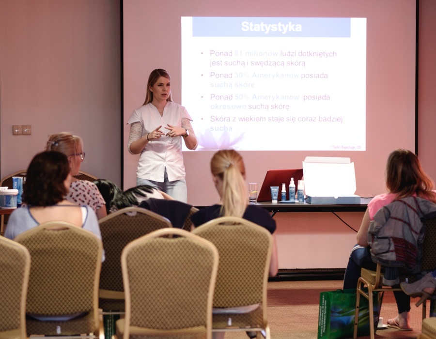 Konferenzraum mit Vortragender, die Hautpflege-Statistiken vor sitzenden Teilnehmern präsentiert