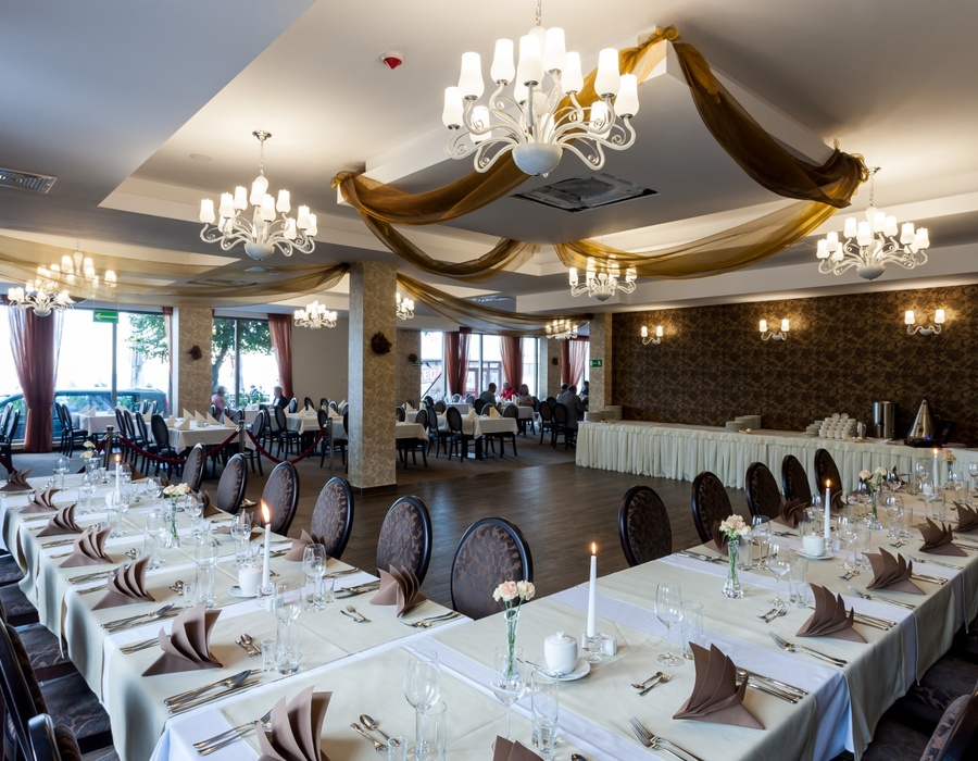 Eleganter Bankettsaal mit weißen Tischdecken, Kerzen, Blumen und Deckenornamenten, bereit für eine Veranstaltung.